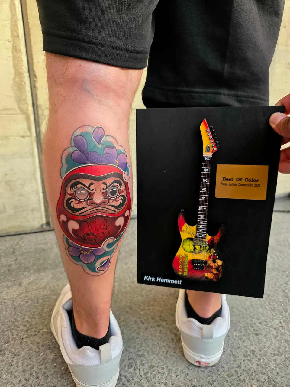 Daruma tatoué sur un mollet, présenté avec une récompense en forme de guitare