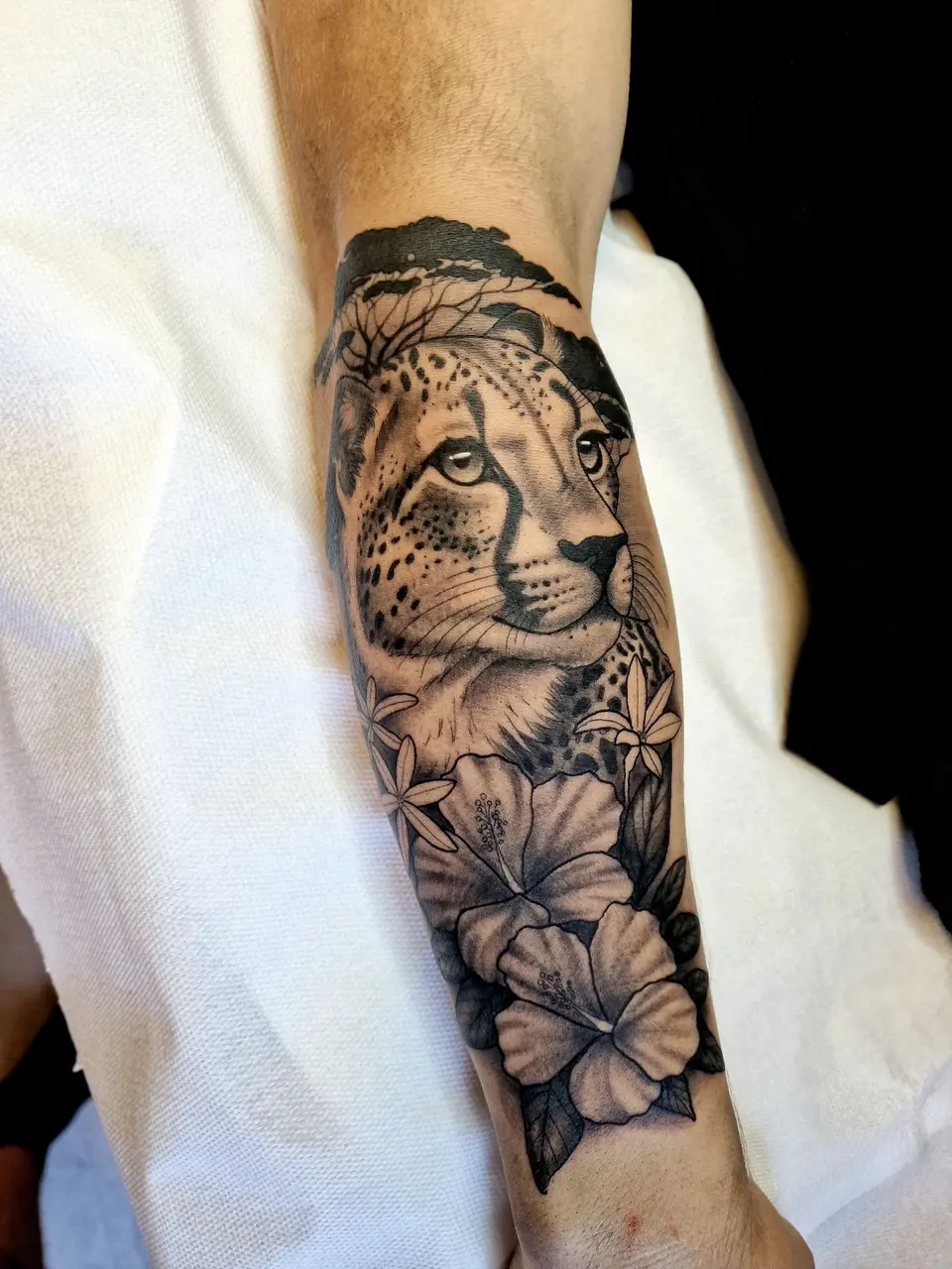 Guépard et fleurs tatoués en noir et gris sur un avant-bras